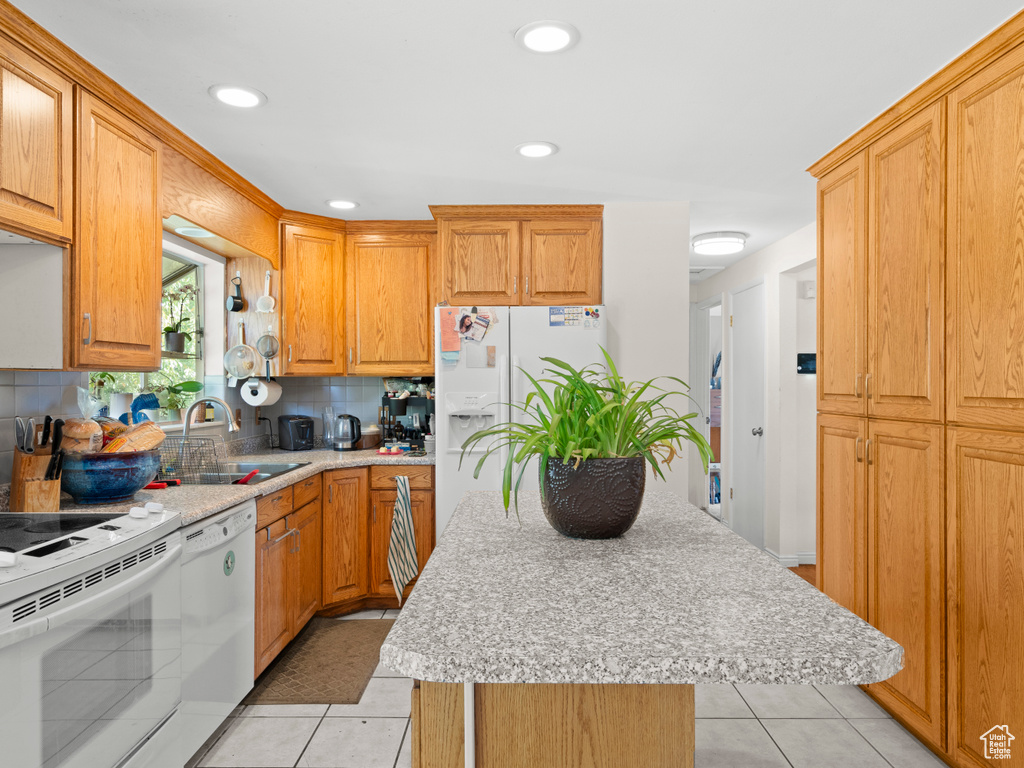 Kitchen with light tile patterned flooring, sink, tasteful backsplash, white appliances, and a kitchen island