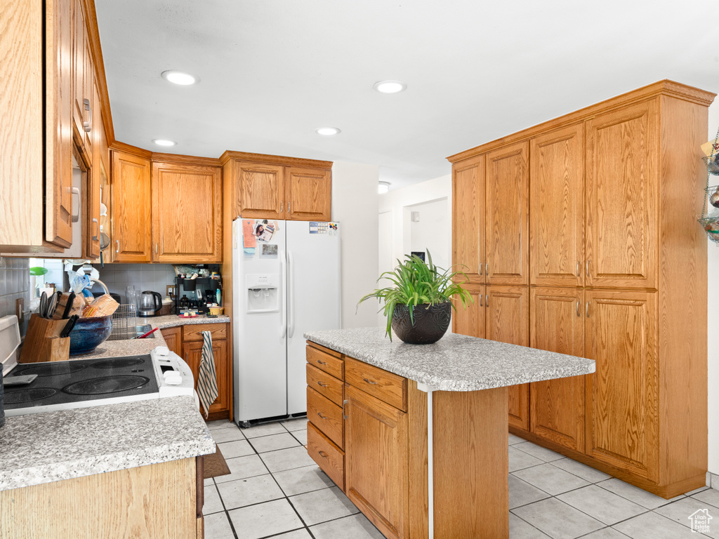 Kitchen featuring white appliances, light tile patterned floors, backsplash, and a center island