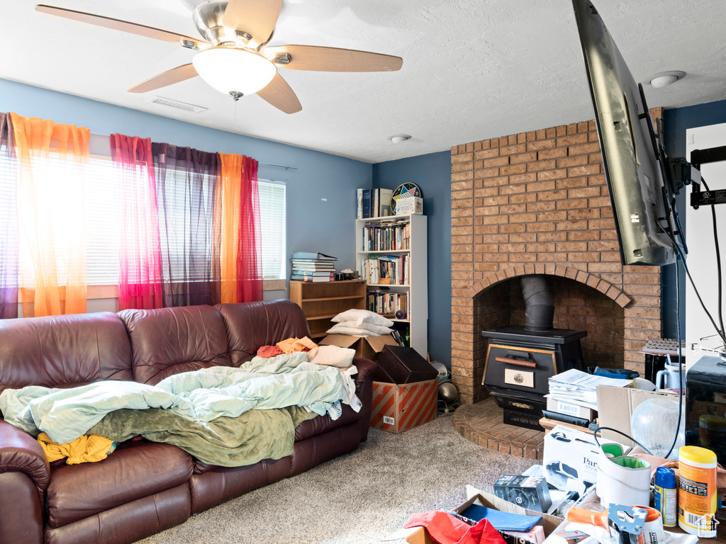 Living room featuring a wood stove, carpet flooring, ceiling fan, and a textured ceiling