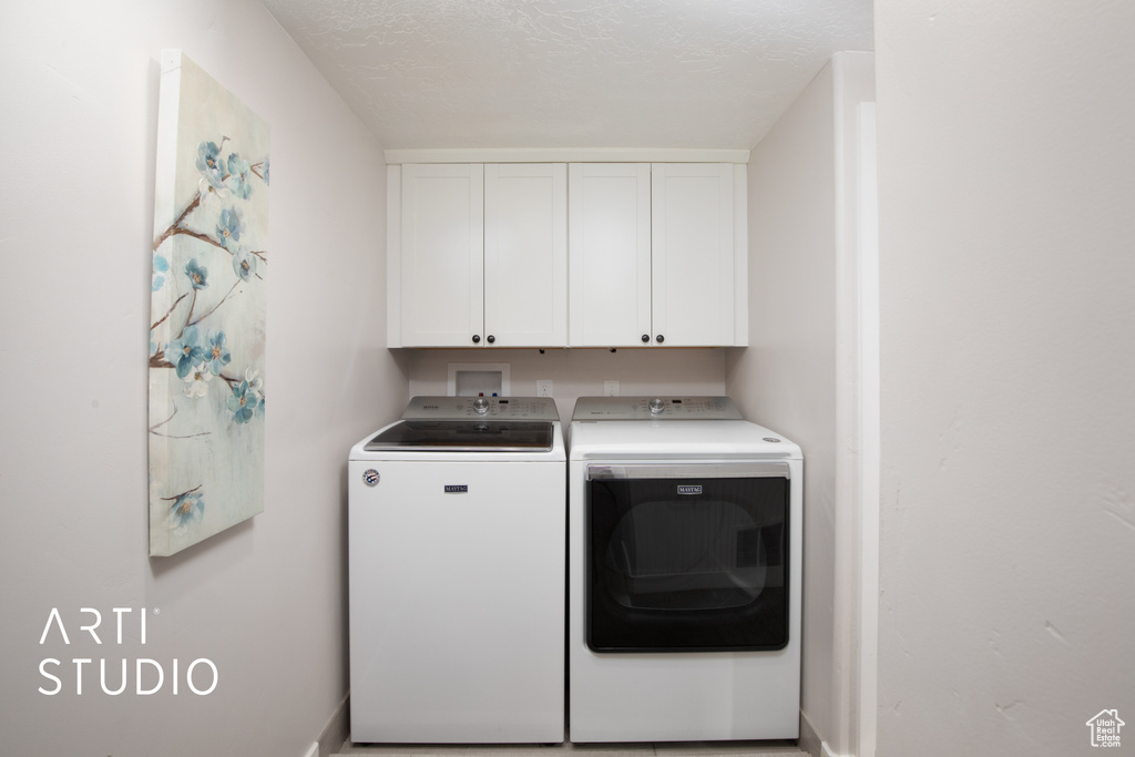 Laundry room featuring cabinets, a textured ceiling, and separate washer and dryer