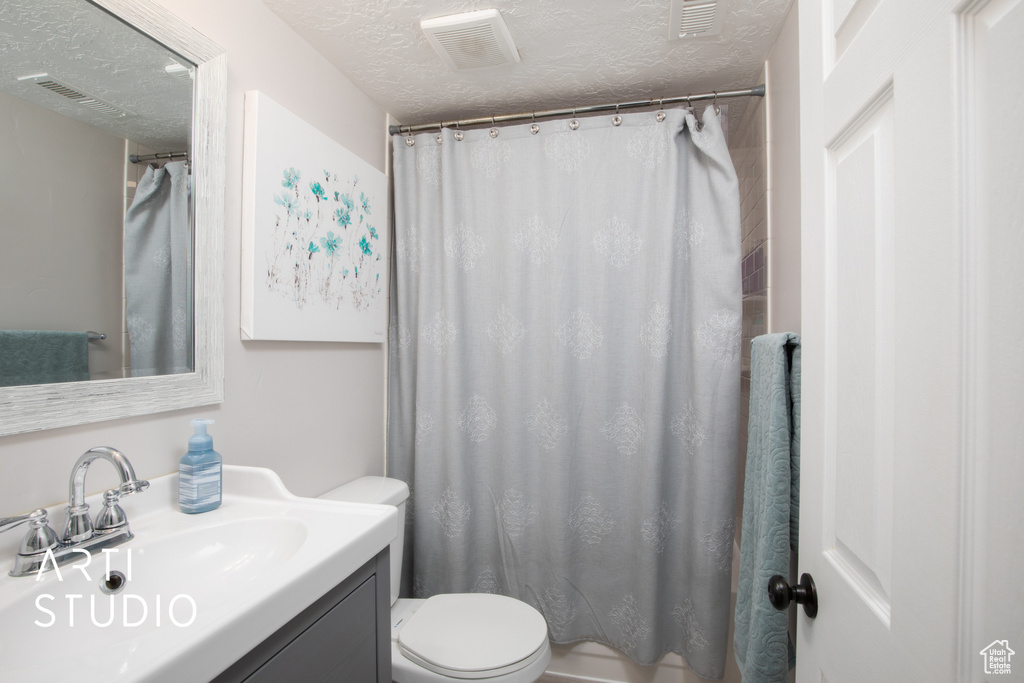 Bathroom featuring vanity, a textured ceiling, toilet, and curtained shower