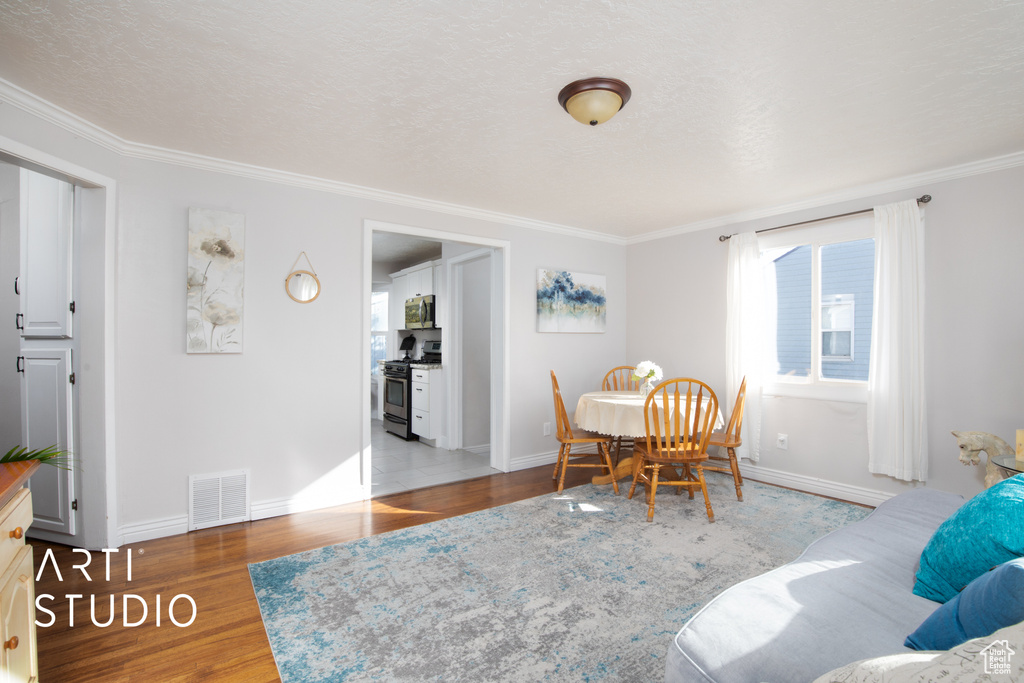 Dining area with hardwood / wood-style floors, a textured ceiling, and ornamental molding