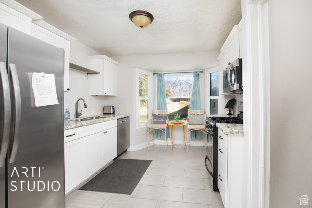 Kitchen with light stone countertops, white cabinetry, sink, and stainless steel appliances