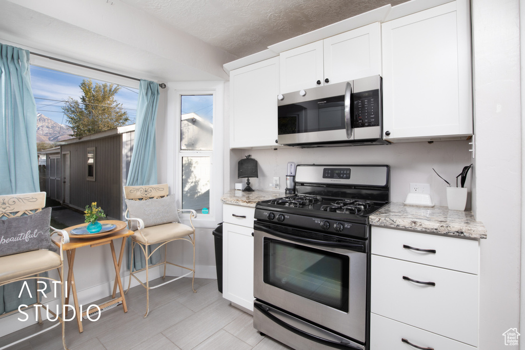 Kitchen featuring white cabinets, appliances with stainless steel finishes, a textured ceiling, and light stone counters