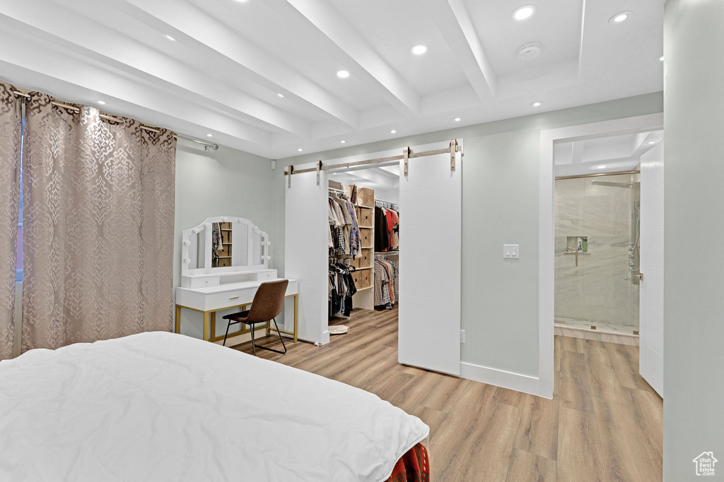 Bedroom featuring a barn door, a spacious closet, beam ceiling, light hardwood / wood-style floors, and a closet