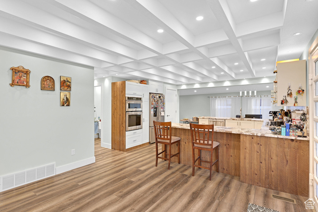 Kitchen with beam ceiling, wood-type flooring, kitchen peninsula, and stainless steel appliances