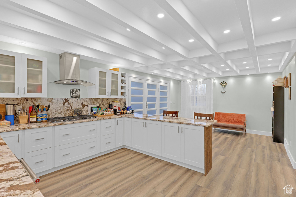 Kitchen with white cabinetry, wall chimney exhaust hood, light stone counters, and stainless steel gas stovetop