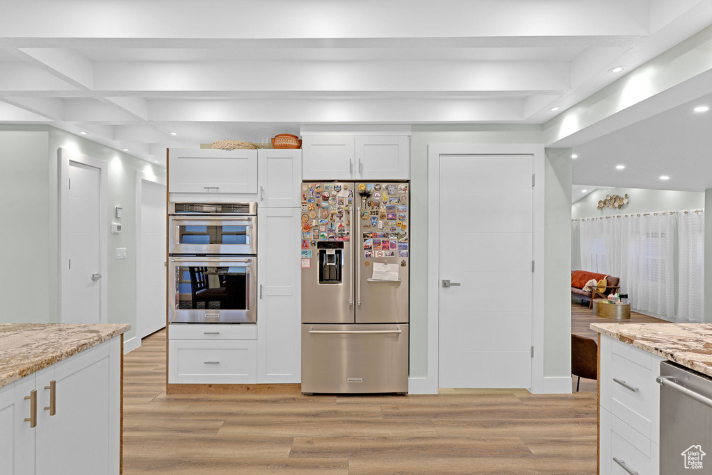 Kitchen featuring white cabinets, light hardwood / wood-style floors, light stone countertops, and appliances with stainless steel finishes