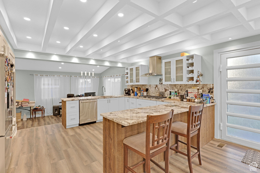 Kitchen featuring kitchen peninsula, white cabinetry, a breakfast bar, and wall chimney range hood