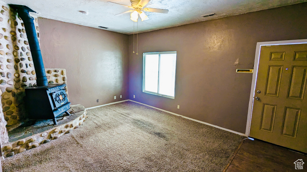 Unfurnished living room with a wood stove, ceiling fan, and dark colored carpet