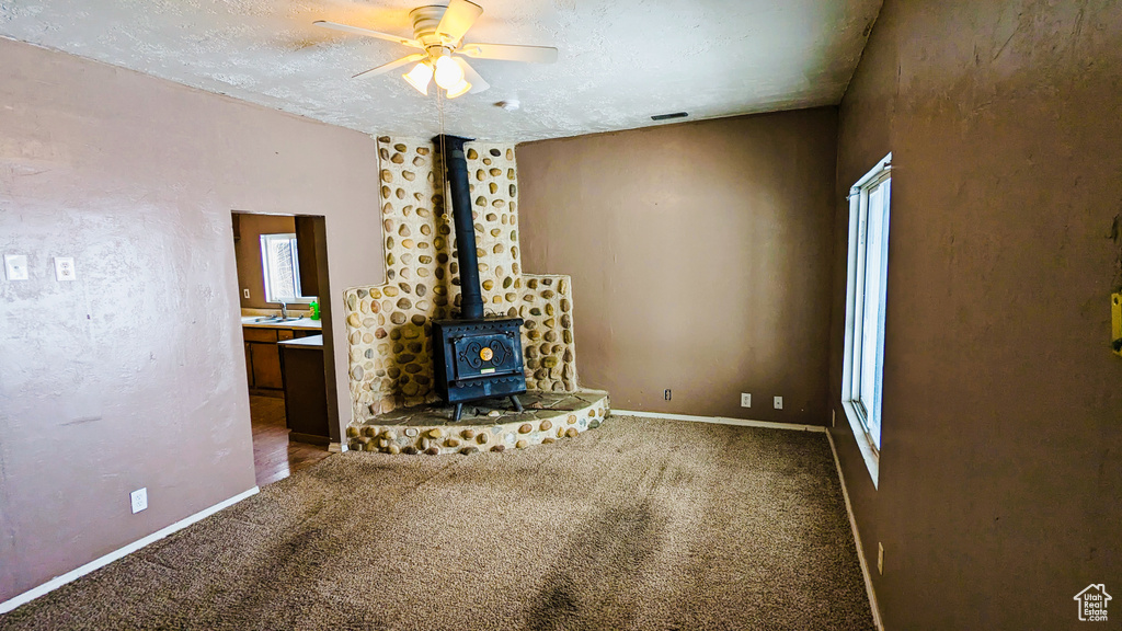 Unfurnished living room featuring carpet flooring, a wood stove, ceiling fan, sink, and a textured ceiling