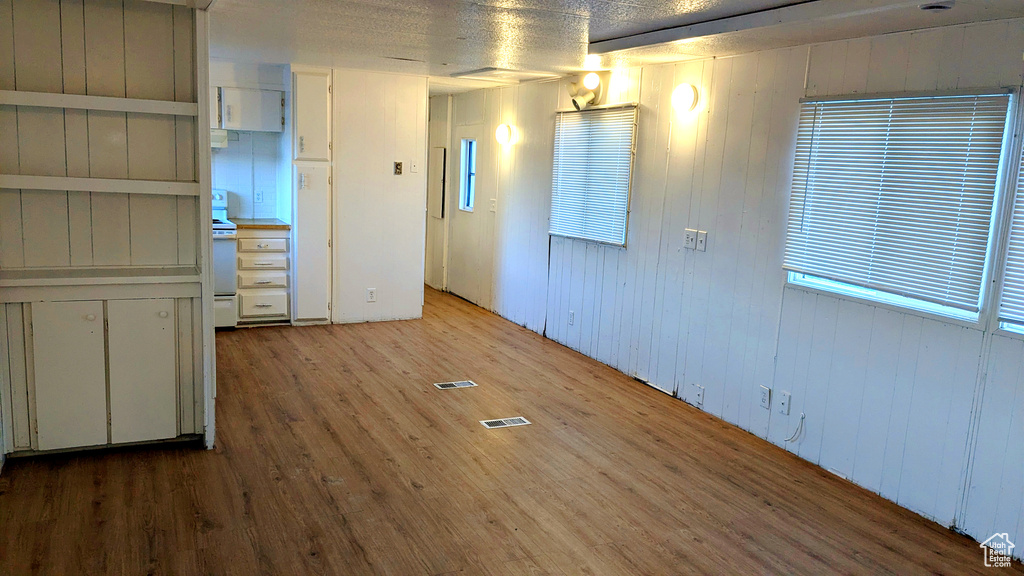 Empty room with wood walls, light hardwood / wood-style floors, and a textured ceiling