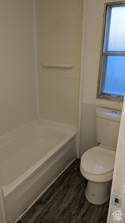 Bathroom with toilet, a bath, and hardwood / wood-style flooring