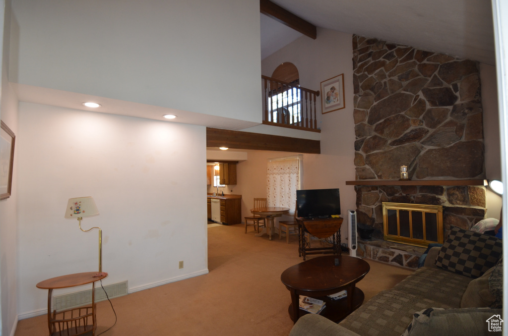 Living room featuring beam ceiling, high vaulted ceiling, light colored carpet, and a stone fireplace