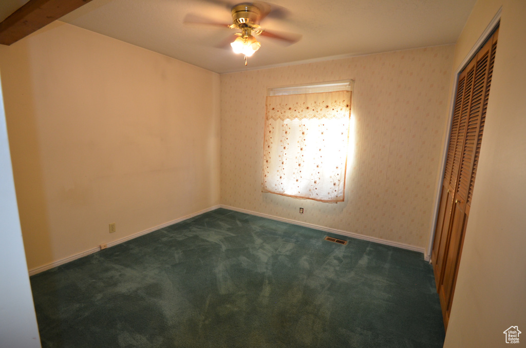 Carpeted spare room featuring beamed ceiling and ceiling fan