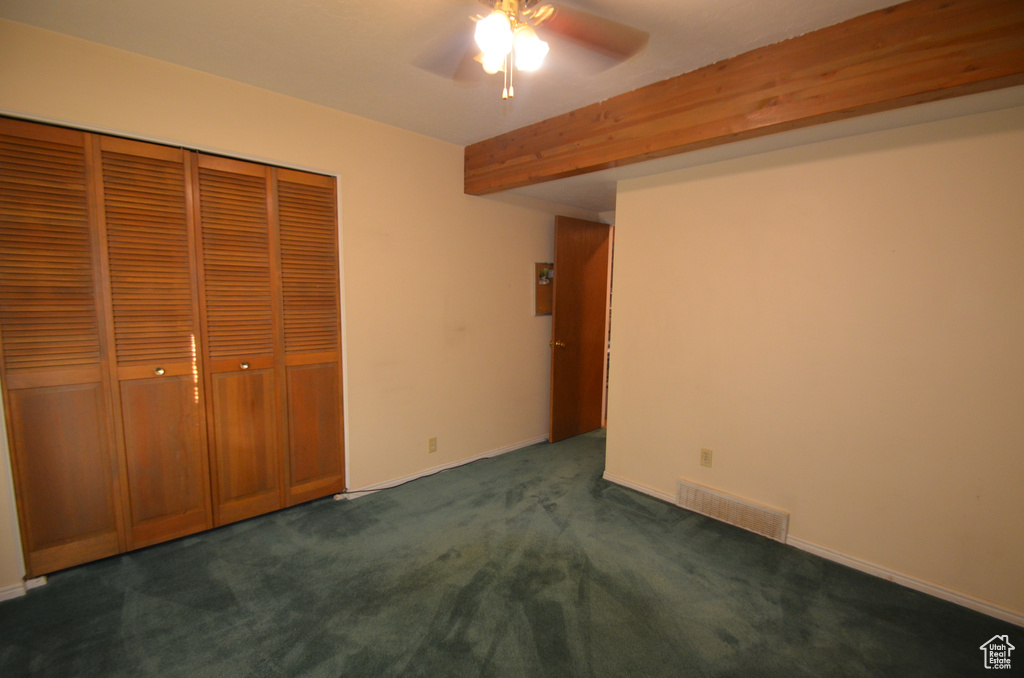 Unfurnished bedroom with dark colored carpet, beam ceiling, a closet, and ceiling fan