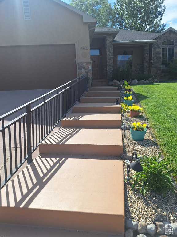 Entrance to property with stone siding, a yard, and a garage