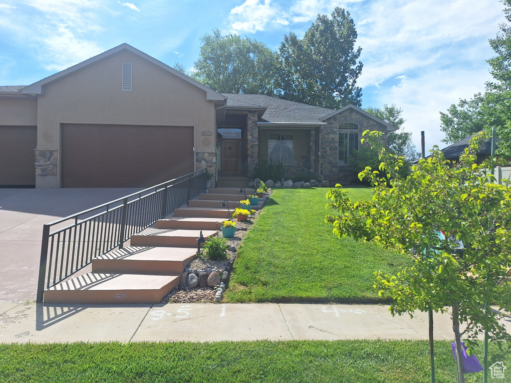 View of front facade featuring stone siding, an attached garage, stucco siding, asphalt driveway, and a front lawn