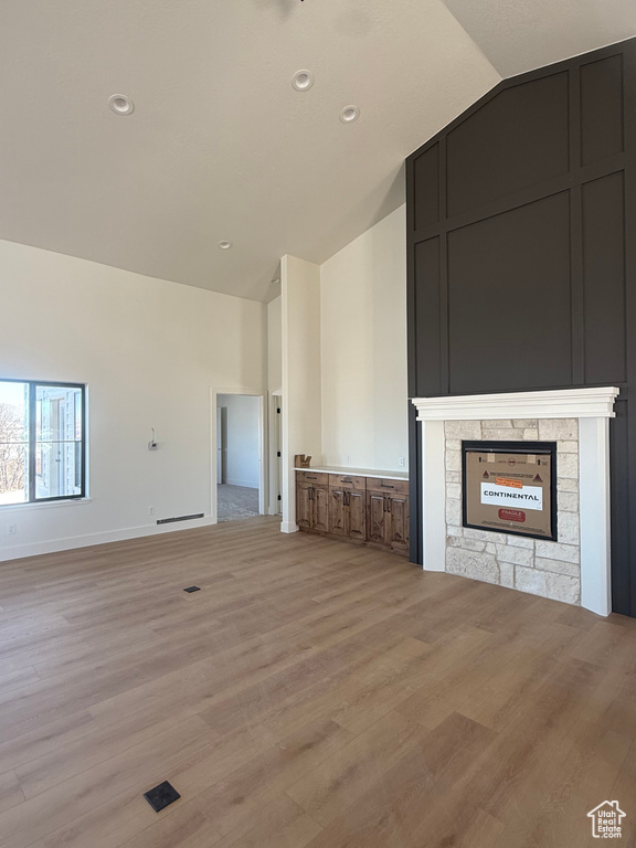 Unfurnished living room with light wood finished floors, baseboards, a stone fireplace, high vaulted ceiling, and recessed lighting