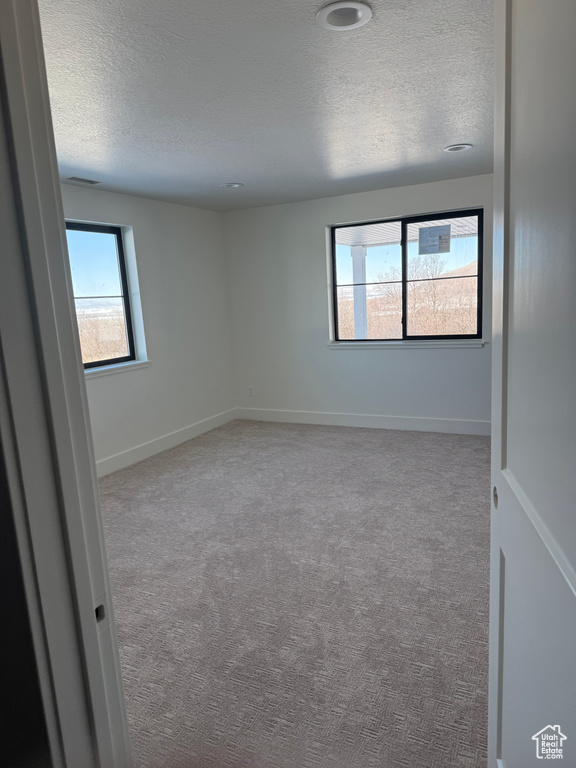 Carpeted empty room with a textured ceiling and baseboards