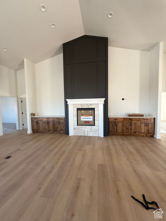 Unfurnished living room with lofted ceiling, light wood finished floors, recessed lighting, and a stone fireplace