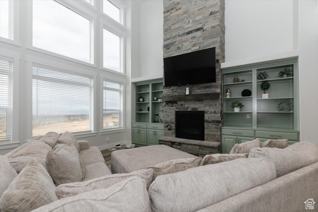 Living room with a stone fireplace, a towering ceiling, a healthy amount of sunlight, and wood-type flooring