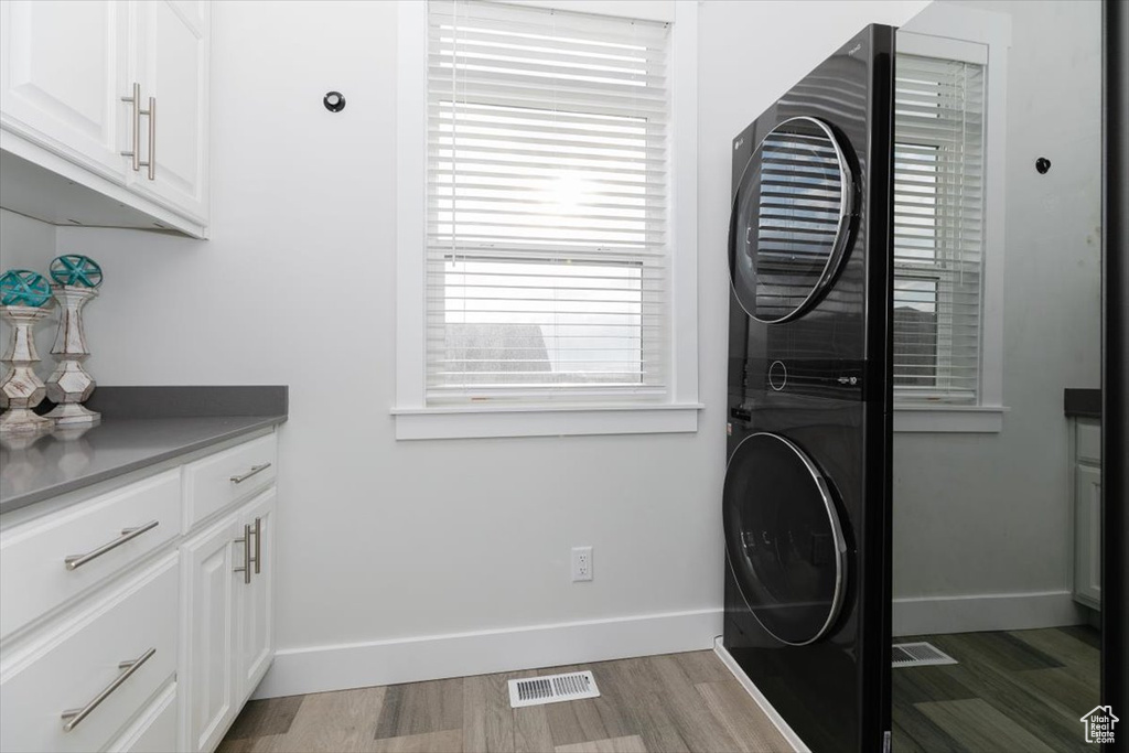 Washroom with stacked washer / dryer, cabinets, and light wood-type flooring