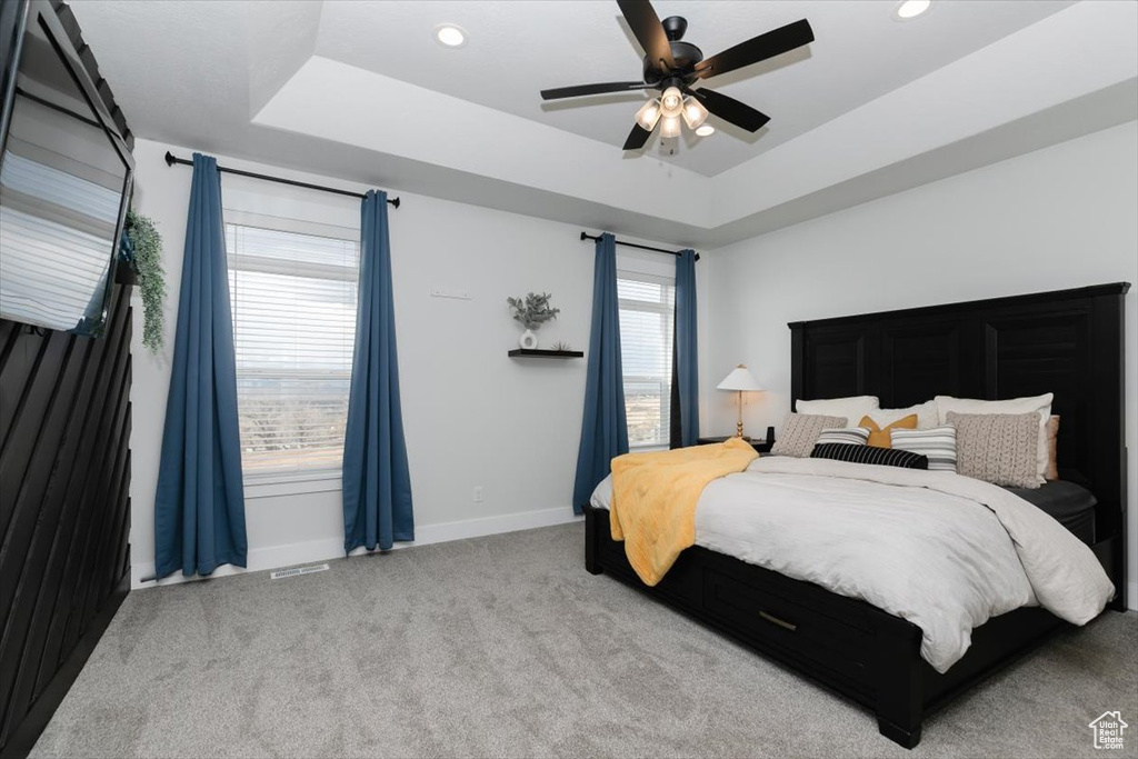 Bedroom featuring a tray ceiling, ceiling fan, and light carpet