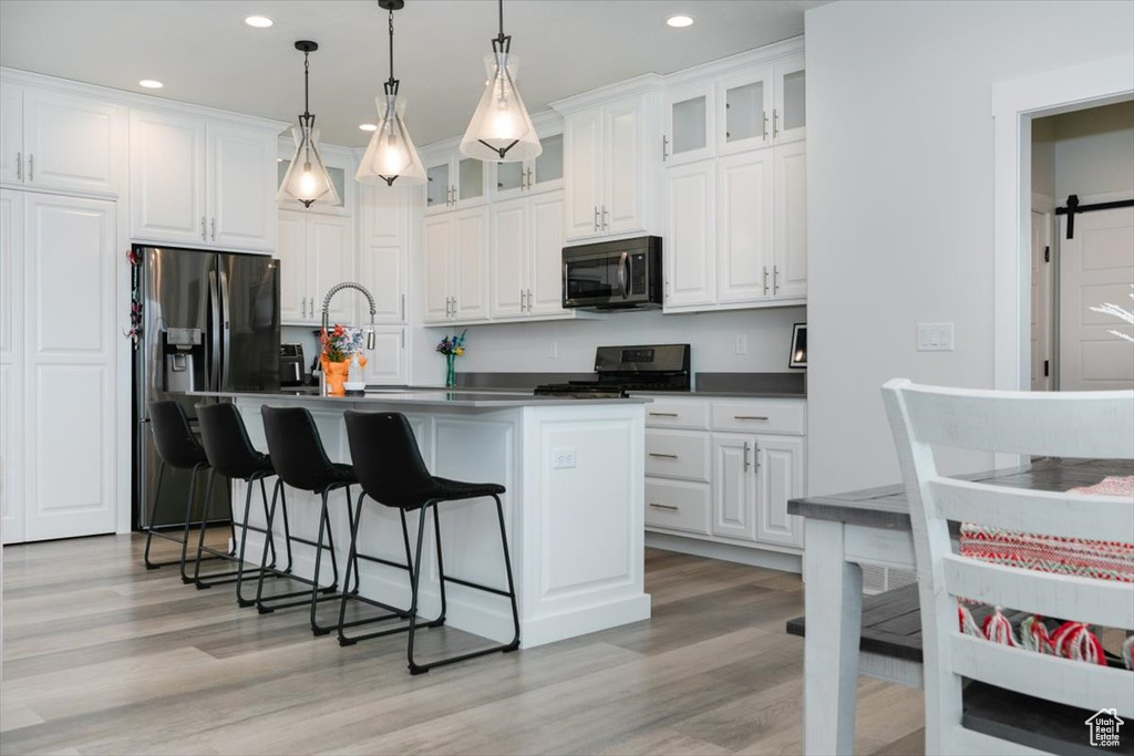 Kitchen with stainless steel appliances, pendant lighting, a barn door, white cabinets, and an island with sink