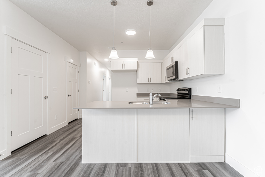 Kitchen with wood finished floors, appliances with stainless steel finishes, light countertops, a sink, and a peninsula
