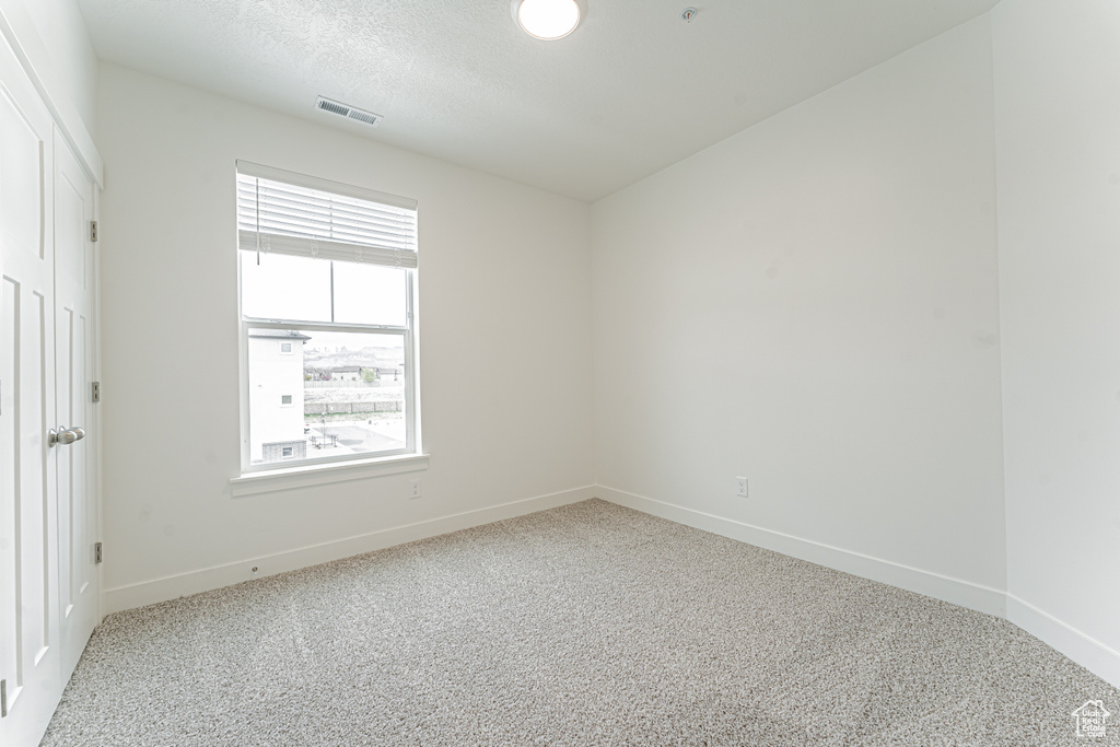 Carpeted empty room with a textured ceiling, visible vents, and baseboards