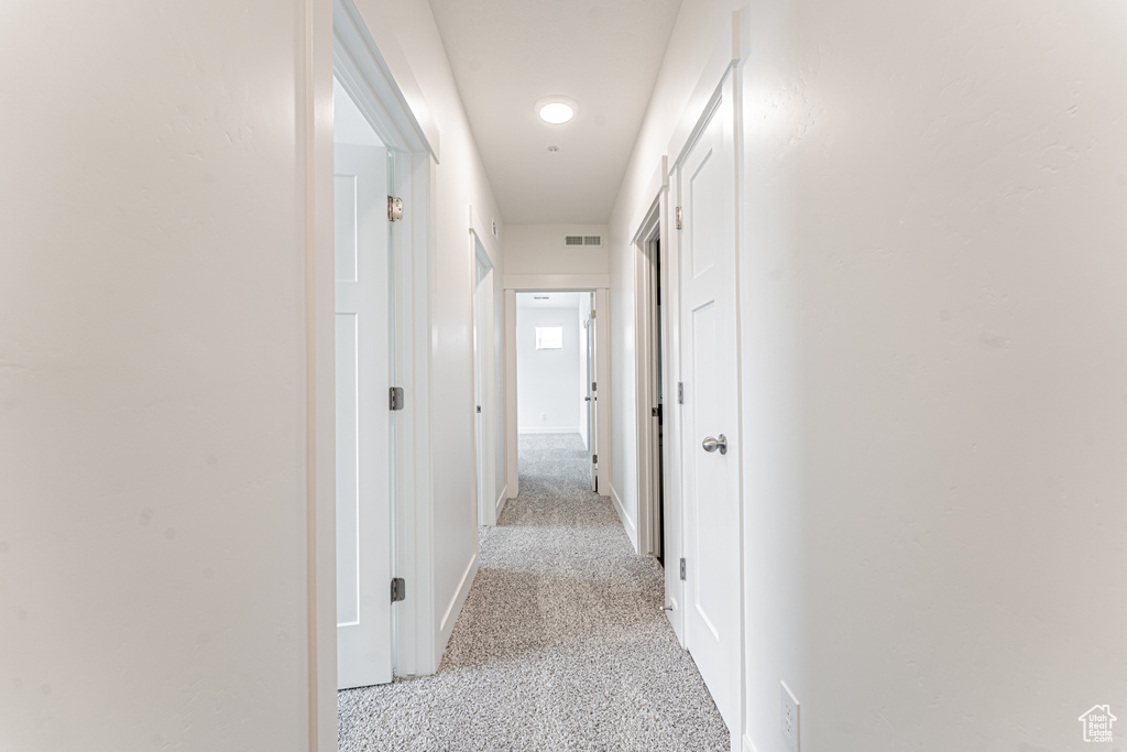 Corridor with baseboards, visible vents, and light colored carpet