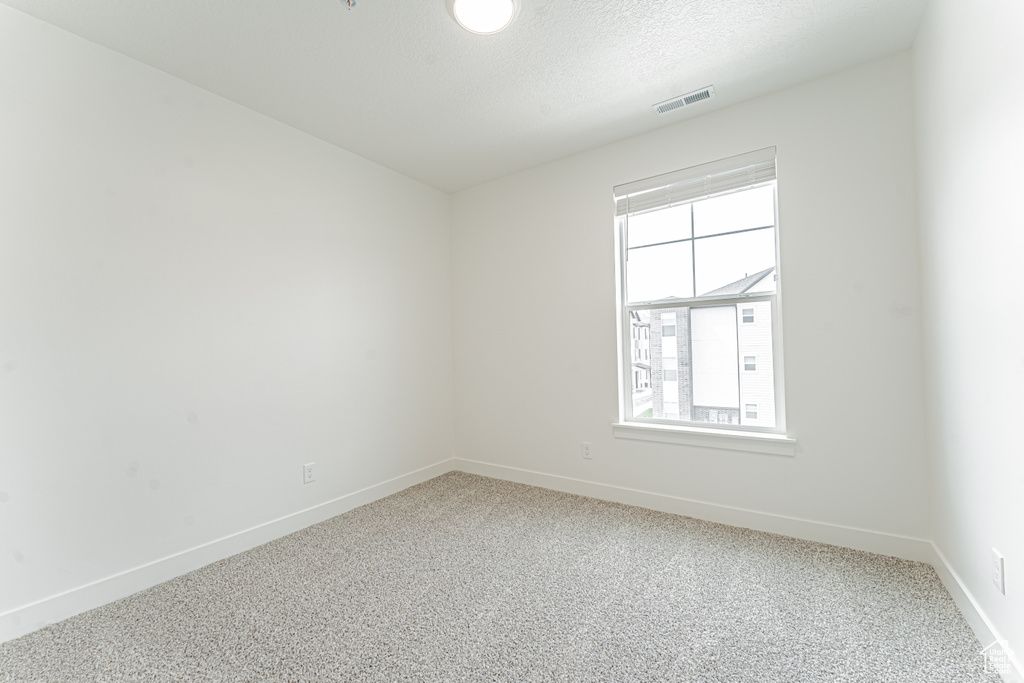 Carpeted empty room featuring baseboards, visible vents, and a textured ceiling