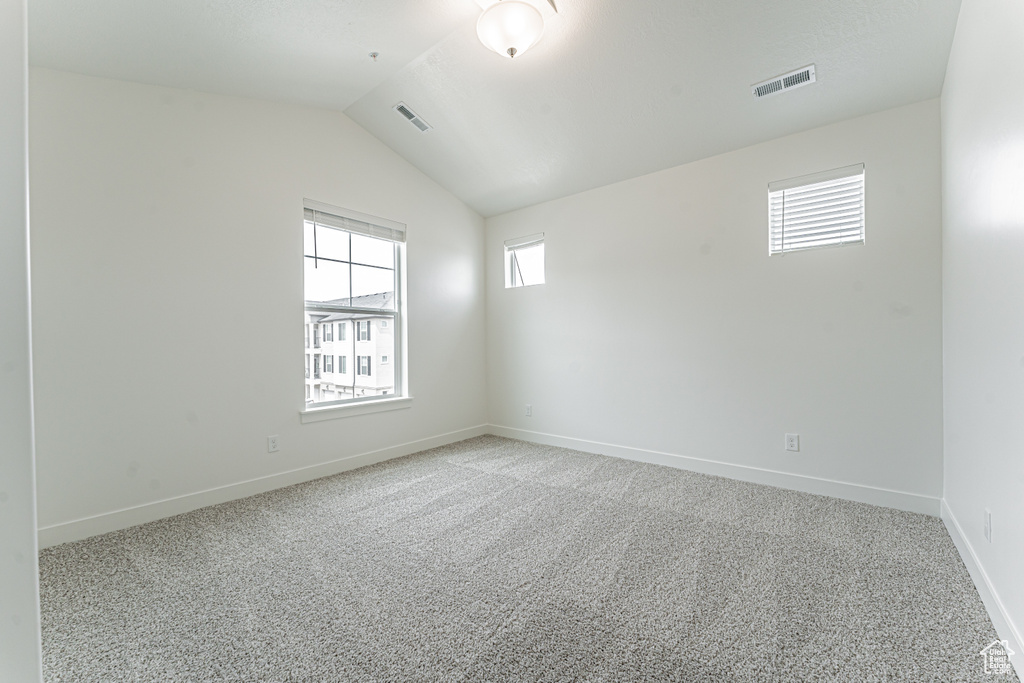 Spare room with lofted ceiling, light colored carpet, visible vents, and baseboards