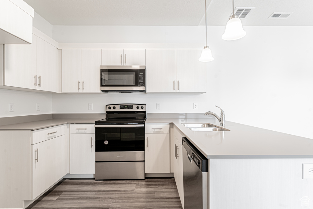 Kitchen with a sink, appliances with stainless steel finishes, visible vents, wood finished floors, and a peninsula