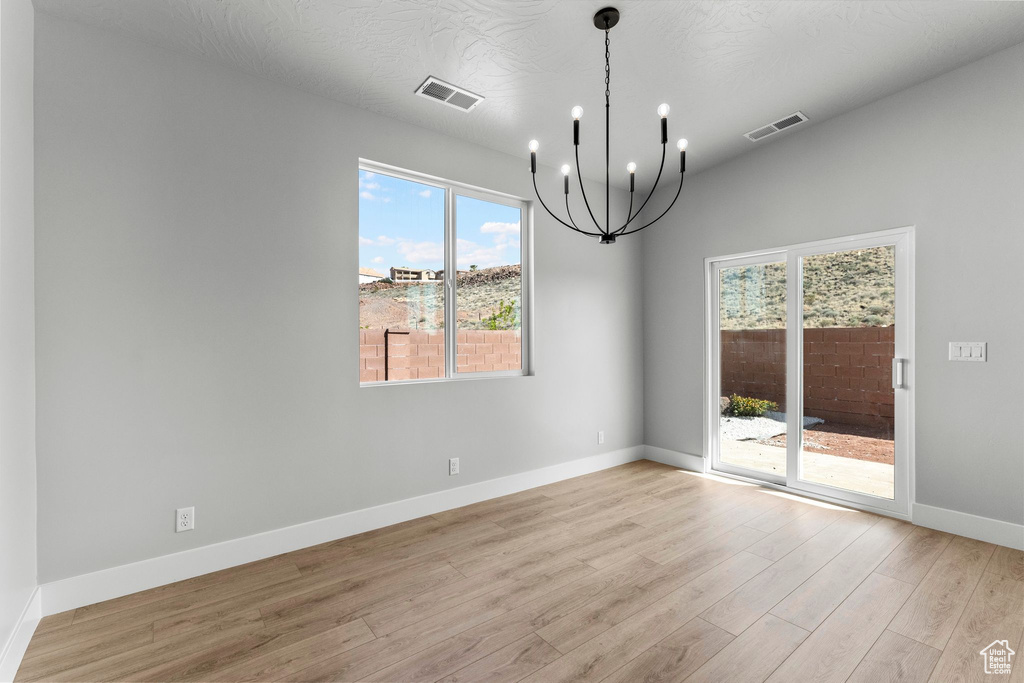 Unfurnished dining area with visible vents, baseboards, a notable chandelier, and light wood-style floors
