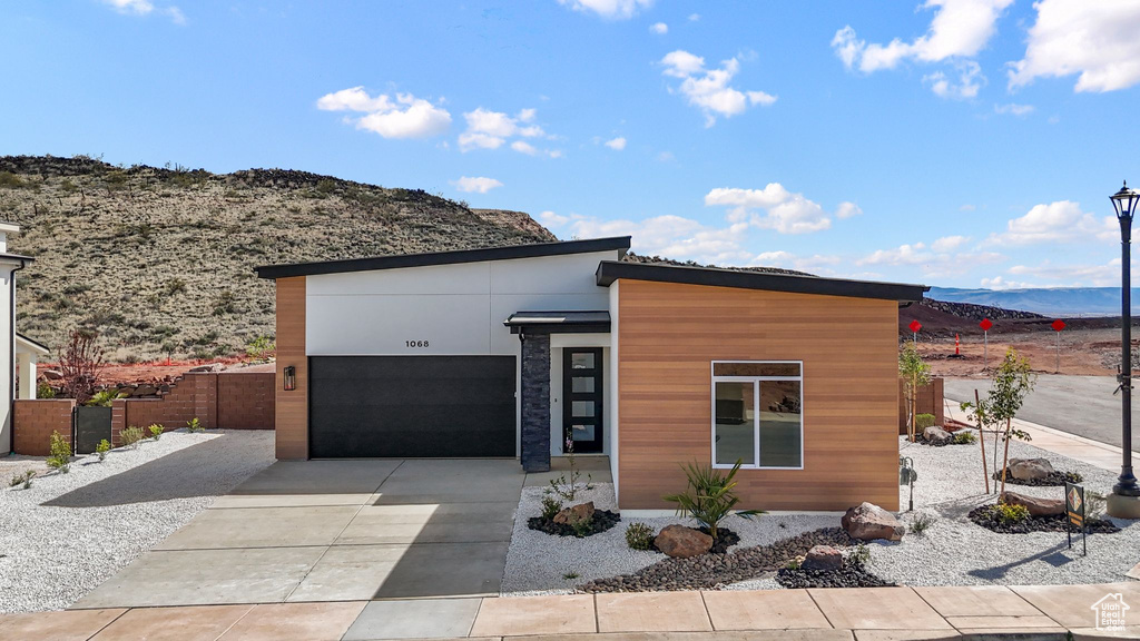 Contemporary house featuring concrete driveway, a mountain view, fence, and a garage