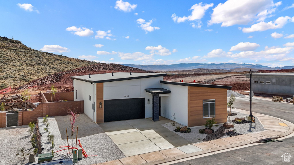 Contemporary house with stucco siding, fence, an attached garage, a mountain view, and concrete driveway