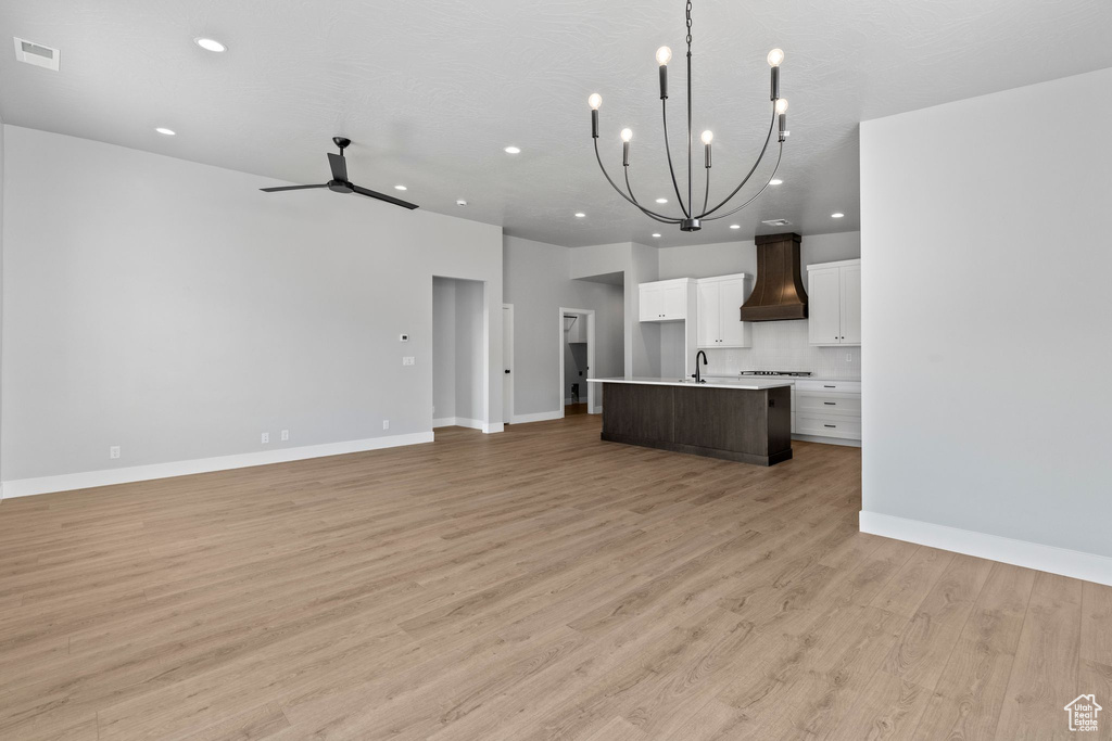 Kitchen featuring custom exhaust hood, open floor plan, visible vents, and a center island with sink