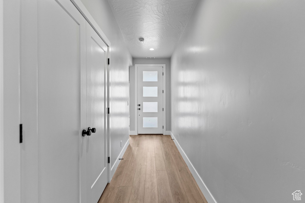 Corridor with light wood-style flooring, a textured ceiling, and baseboards