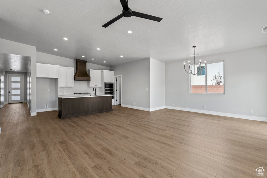 Kitchen with a sink, baseboards, premium range hood, and ceiling fan with notable chandelier