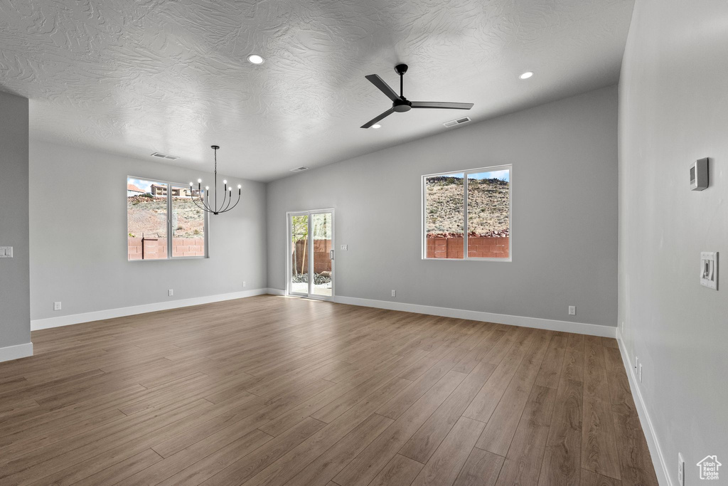 Spare room with wood finished floors, ceiling fan with notable chandelier, baseboards, and visible vents
