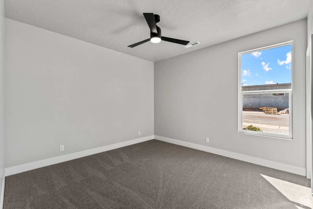 Unfurnished room with dark carpet, plenty of natural light, and visible vents