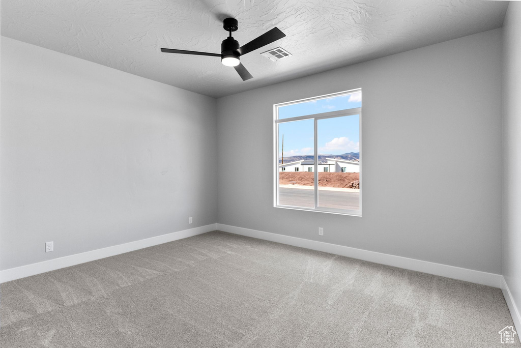 Carpeted empty room featuring a textured ceiling, baseboards, a ceiling fan, and visible vents