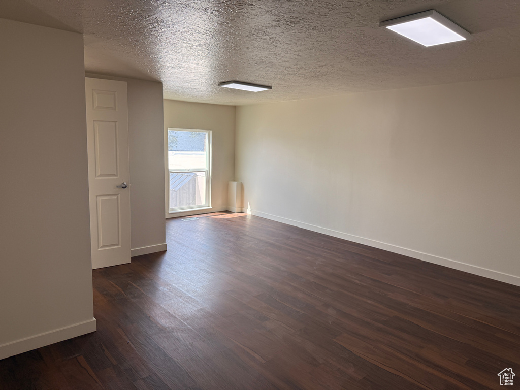 Spare room with baseboards, a textured ceiling, and dark wood-style flooring