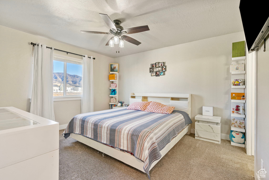 Bedroom with a textured ceiling, light colored carpet, and ceiling fan