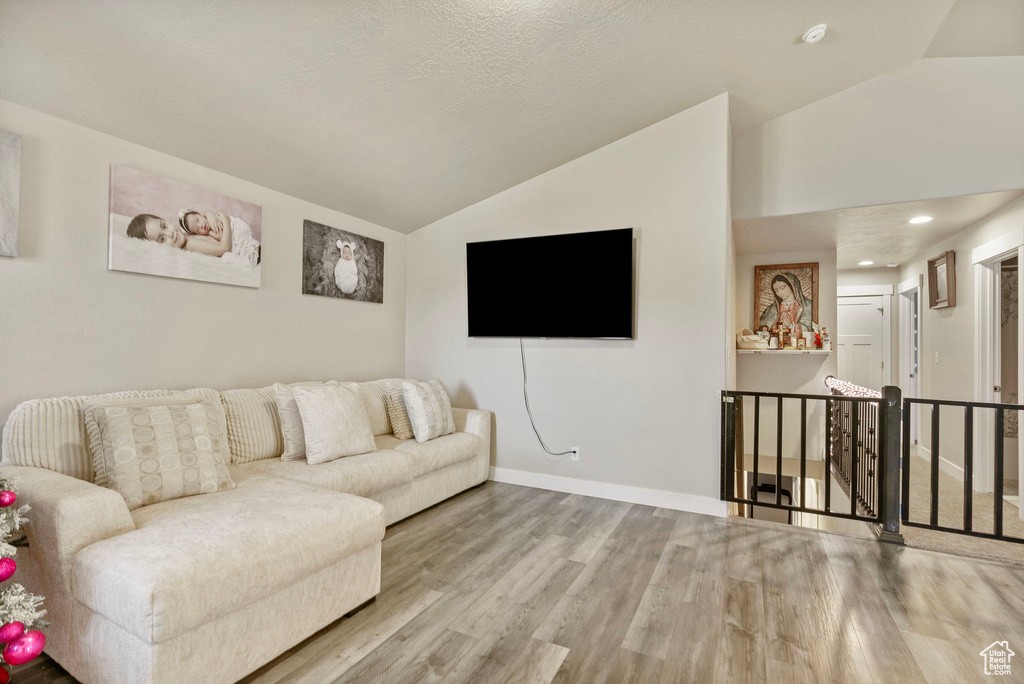 Living room with a textured ceiling, light hardwood / wood-style floors, and lofted ceiling