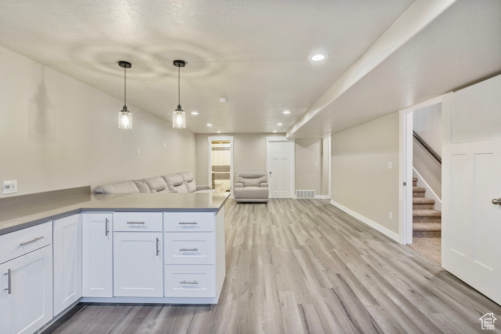 Kitchen with kitchen peninsula, a textured ceiling, light hardwood / wood-style floors, white cabinetry, and hanging light fixtures