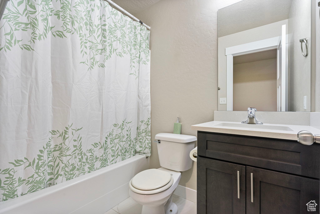 Full bathroom featuring a textured ceiling, vanity, shower / bathtub combination with curtain, tile patterned flooring, and toilet