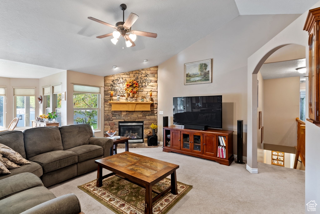 Living room featuring ceiling fan, a stone fireplace, lofted ceiling, and light carpet